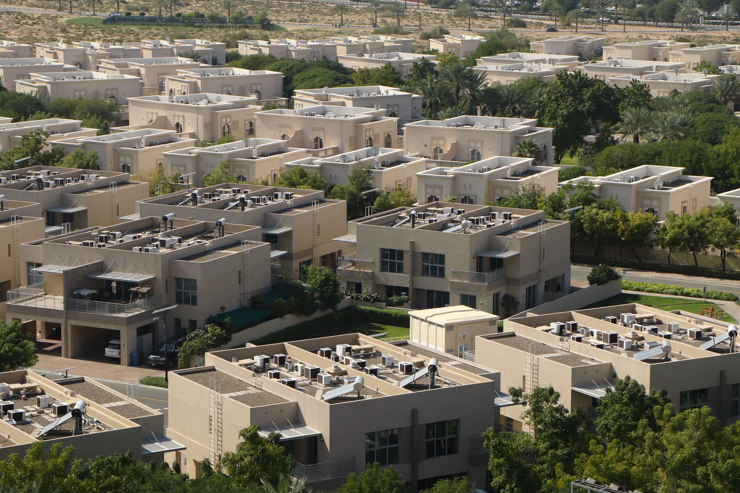 Rows of sand-coloured villas with rooftop plant and walled gardens in a Dubai community, seen from above