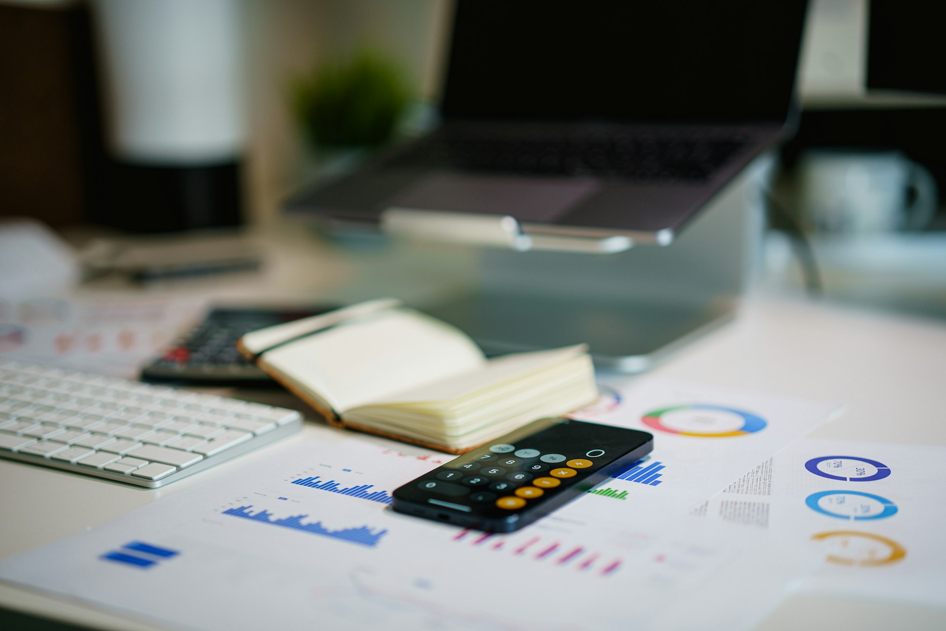 A desk with a laptop, calculator and printed financial charts